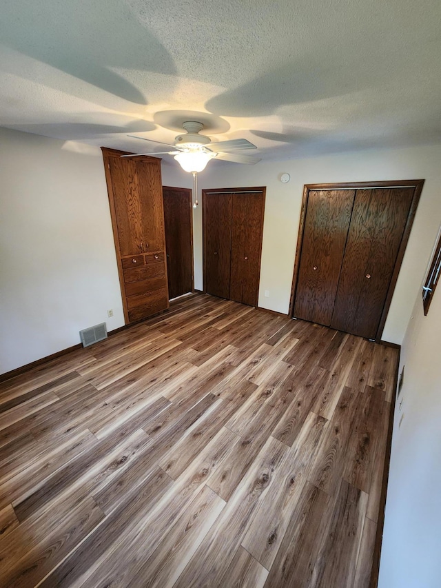 1180 Hathaway Ln NE, Fridley, MN 55432 - unfurnished bedroom featuring wood finished floors, two closets, a textured ceiling, and a ceiling fan