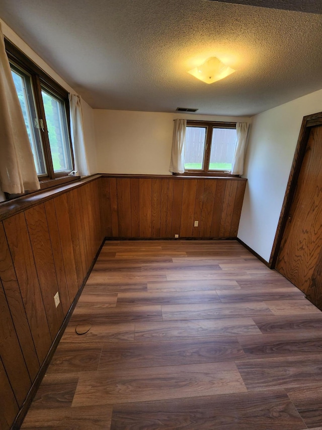 1180 Hathaway Ln NE, Fridley, MN 55432 - spare room featuring dark wood finished floors, healthy amount of natural light, a textured ceiling, wooden walls, and a wainscoted wall