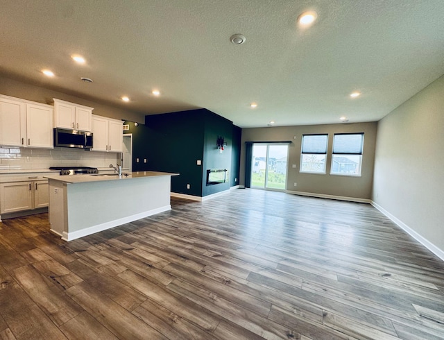 5022 Useppa Trl, Woodbury, MN 55129 - kitchen featuring stainless steel microwave, a kitchen island with sink, dark wood finished floors, decorative backsplash, and recessed lighting