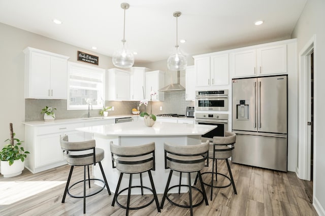 6016 Inskip Ave S, Cottage Grove, MN 55016 - kitchen with stainless steel appliances, wall chimney range hood, a kitchen island, light wood-style flooring, and white cabinets