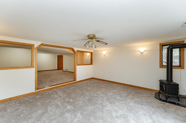 2310 Wilshire Ln NE, Rochester, MN 55906 - unfurnished living room featuring a wood stove, ceiling fan, carpet floors, and baseboards