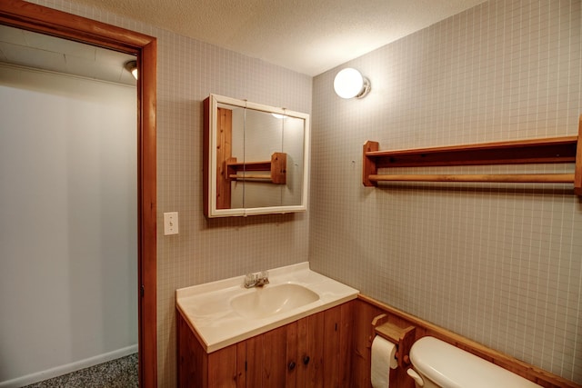 14070 County 18, Park Rapids, MN 56470 - bathroom with toilet, vanity, wallpapered walls, a textured ceiling, and baseboards