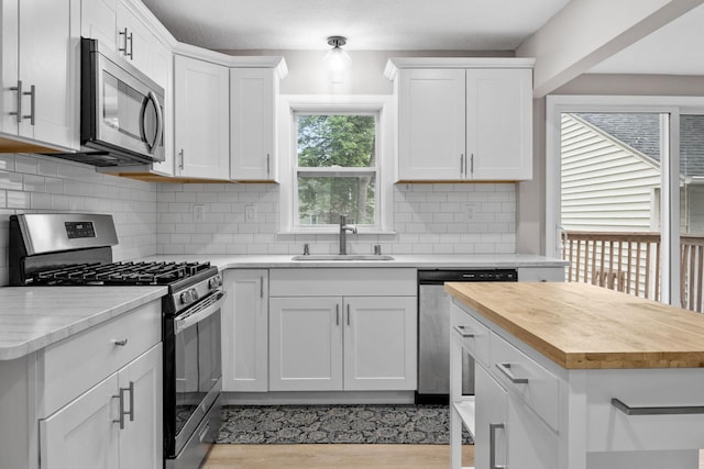 5814 Ewing Ave N, Brooklyn Center, MN 55429 - kitchen featuring stainless steel appliances, wooden counters, light wood-style floors, white cabinetry, and backsplash