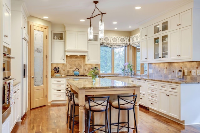 10025 Adam Ave, Inver Grove Heights, MN 55077 - kitchen featuring a kitchen bar, light wood-style flooring, white cabinetry, a center island, and backsplash