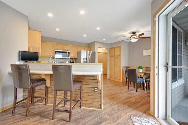 6103 150th St N, Hugo, MN 55038 - kitchen featuring appliances with stainless steel finishes, light brown cabinetry, a peninsula, light wood-style floors, and a kitchen breakfast bar