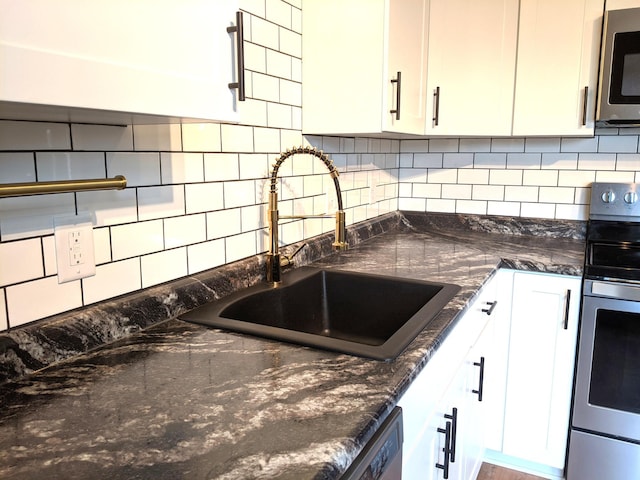 1101 Spring Creek Rd, Northfield, MN 55057 - kitchen featuring appliances with stainless steel finishes, a sink, white cabinetry, tasteful backsplash, and dark stone counters