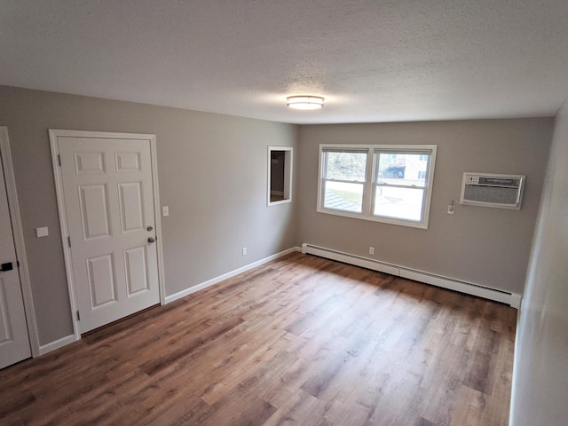 1101 Spring Creek Rd, Northfield, MN 55057 - unfurnished room featuring baseboard heating, a wall mounted AC, wood finished floors, a textured ceiling, and baseboards