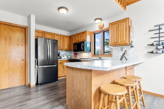 13771 Schuelke Beach Rd NW, Leaf Valley Twp, MN 56354 - kitchen featuring black appliances, wood finished floors, a peninsula, a breakfast bar area, and decorative backsplash