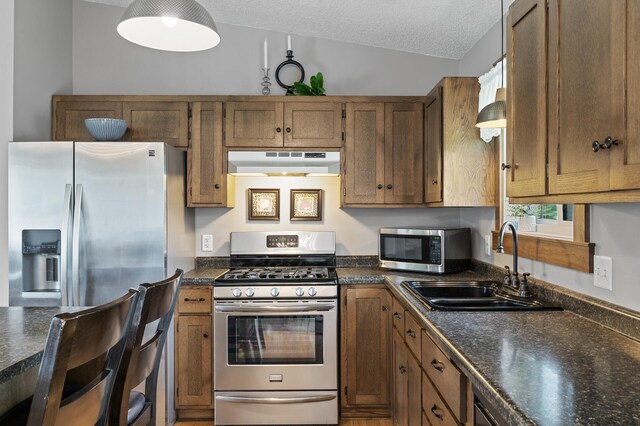 18125 Fillmore St NE, East Bethel, MN 55011 - kitchen featuring appliances with stainless steel finishes, under cabinet range hood, dark countertops, brown cabinetry, and a textured ceiling