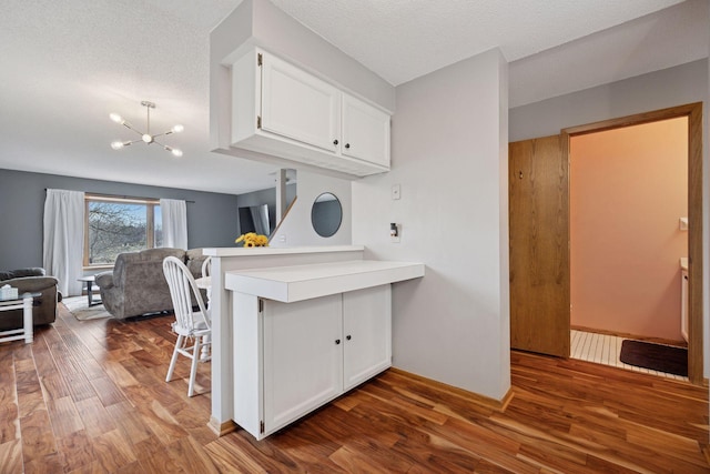 2436 Mendelssohn Ln N, Golden Valley, MN 55427 - kitchen featuring wood finished floors, white cabinets, open floor plan, a peninsula, and a chandelier