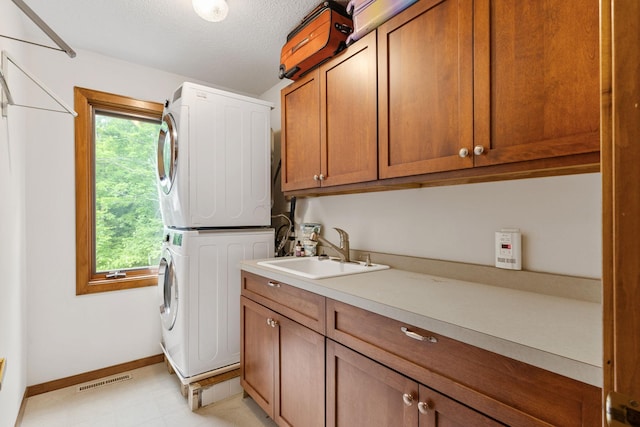 10390 Fenner Ave SE, Franklin Twp, MN 55328 - laundry area featuring estacked washer and dryer, cabinet space, baseboards, and a textured ceiling