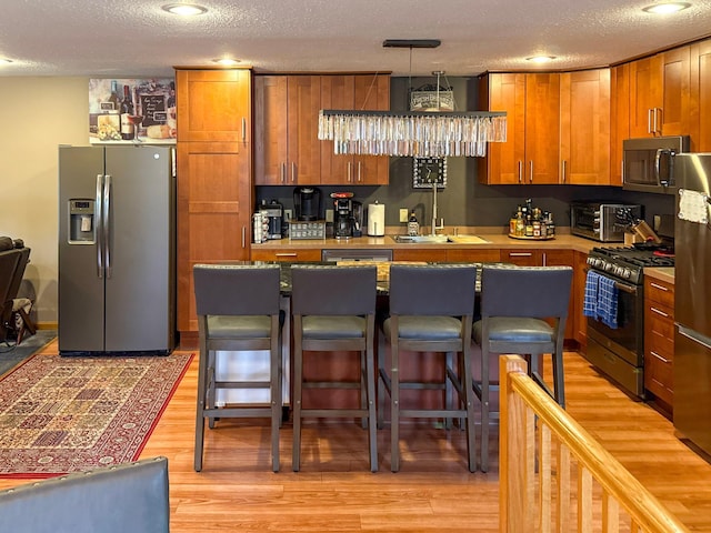 922 Whiskey Rd NW, Isanti, MN 55040 - kitchen featuring stainless steel appliances, a sink, a textured ceiling, light wood-type flooring, and a breakfast bar