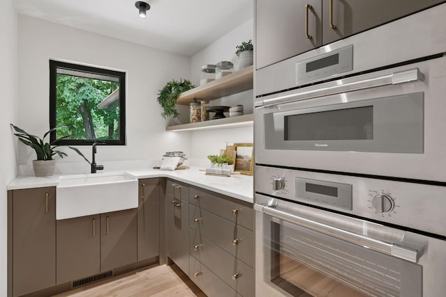 6608 Pawnee Rd, Edina, MN 55439 - kitchen with gray cabinetry, light wood-style floors, open shelves, light stone counters, and double oven