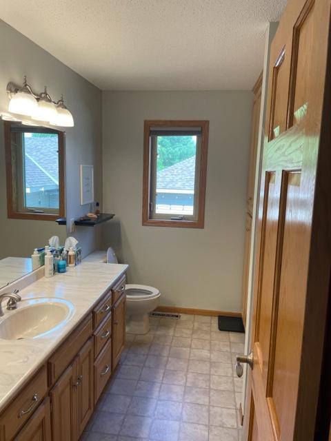 409 Iris Ln NE, Saint Joseph, MN 56374 - bathroom featuring toilet, vanity, a textured ceiling, and baseboards