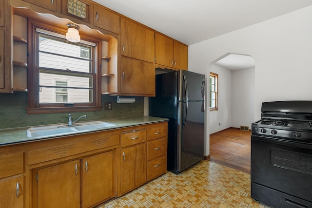 1306 6th Ave NW, Austin, MN 55912 - kitchen featuring black appliances, arched walkways, open shelves, brown cabinetry, and light countertops
