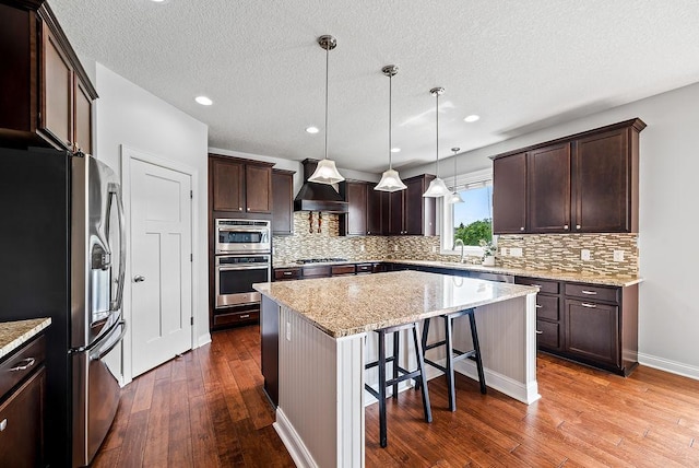 10388 188th St W, Lakeville, MN 55044 - kitchen with stainless steel appliances, premium range hood, dark wood-style flooring, a center island, and dark brown cabinetry