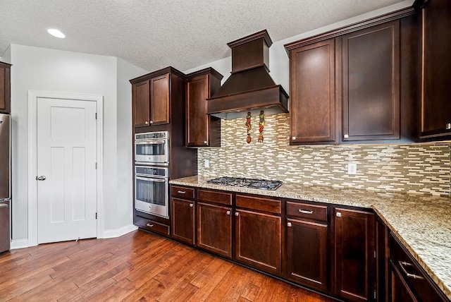 10388 188th St W, Lakeville, MN 55044 - kitchen featuring custom range hood, appliances with stainless steel finishes, dark wood-style floors, light stone countertops, and backsplash
