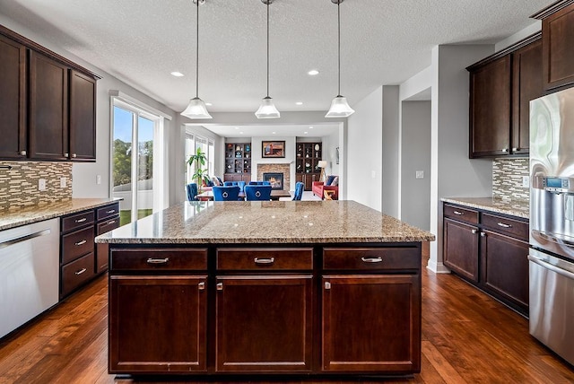 10388 188th St W, Lakeville, MN 55044 - kitchen featuring appliances with stainless steel finishes, a fireplace, dark wood-style floors, decorative backsplash, and light stone counters