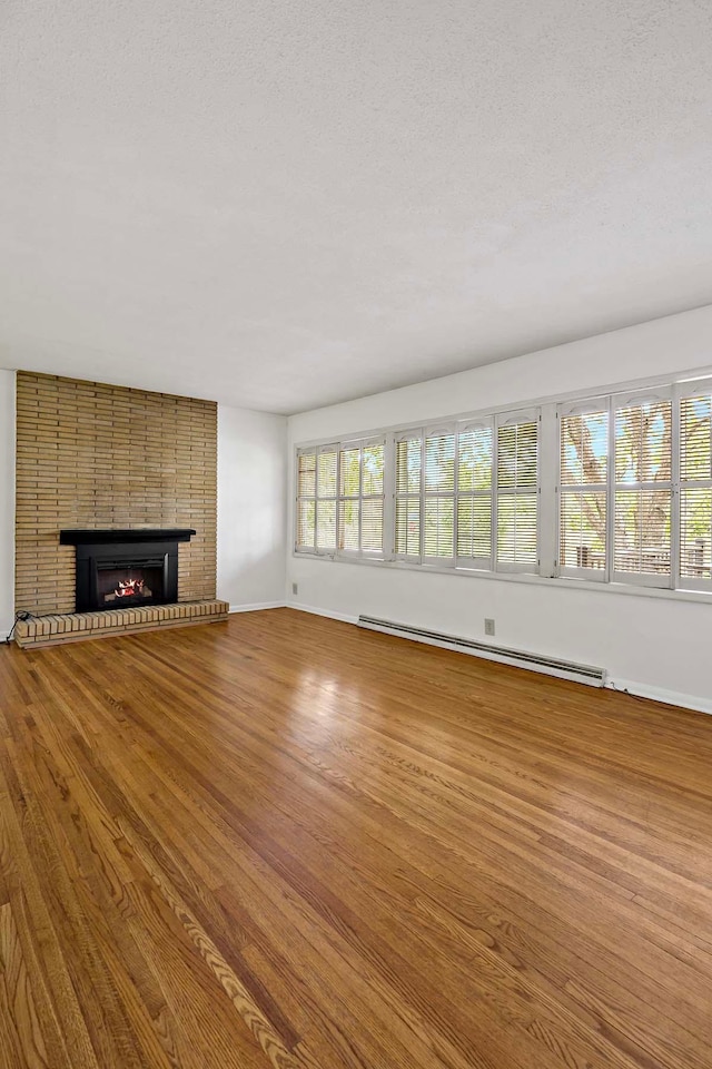 3671 Robinwood Ter, Minnetonka, MN 55305 - unfurnished living room with a baseboard heating unit, wood finished floors, baseboards, a fireplace, and a textured ceiling