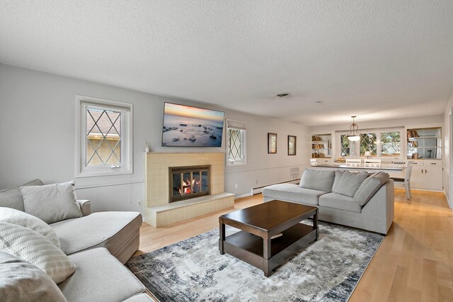 3004 36th Ave NE, Saint Anthony, MN 55418 - living room featuring a textured ceiling, healthy amount of natural light, a tiled fireplace, light wood-type flooring, and baseboard heating