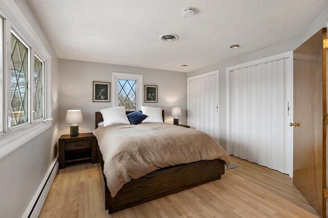 3004 36th Ave NE, Saint Anthony, MN 55418 - bedroom with a baseboard radiator, a textured ceiling, light wood-style floors, baseboards, and two closets