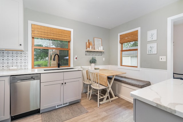 2211 108th Ave NW, Coon Rapids, MN 55433 - kitchen featuring stainless steel dishwasher, a sink, light wood-style flooring, light stone countertops, and a wainscoted wall