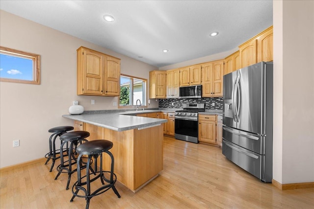 1195 64th St, Hudson, WI 54016 - kitchen with stainless steel appliances, a peninsula, a kitchen breakfast bar, tasteful backsplash, and light wood-style flooring