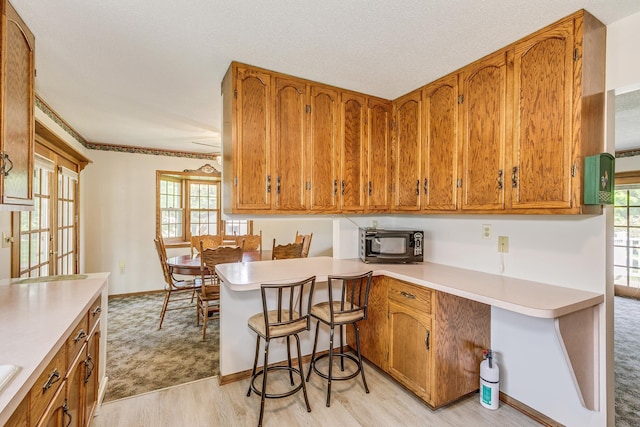 10275 Park Cir, Pine City, MN 55063 - kitchen with black microwave, brown cabinets, light countertops, light wood-type flooring, and a peninsula
