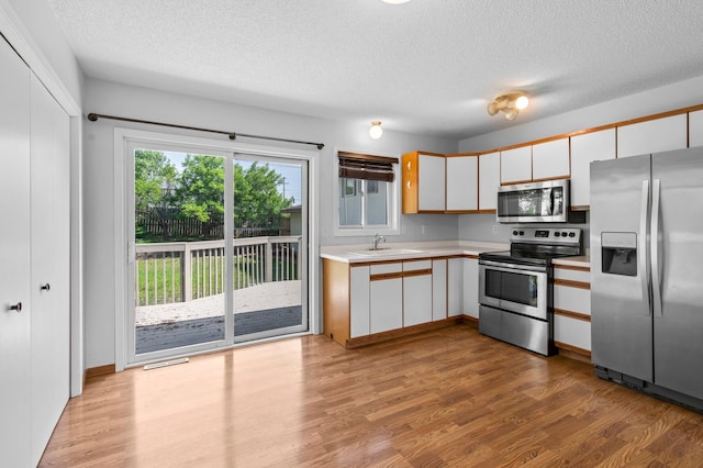 2125 White Bear Ave N, Maplewood, MN 55109 - kitchen featuring stainless steel appliances, light countertops, a textured ceiling, light wood-style flooring, and white cabinets
