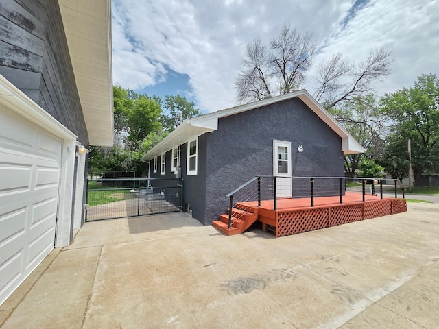 4106 Woodbine Ln N, Brooklyn Center, MN 55429 - view of home's exterior with stucco siding, a wooden deck, a gate, and driveway