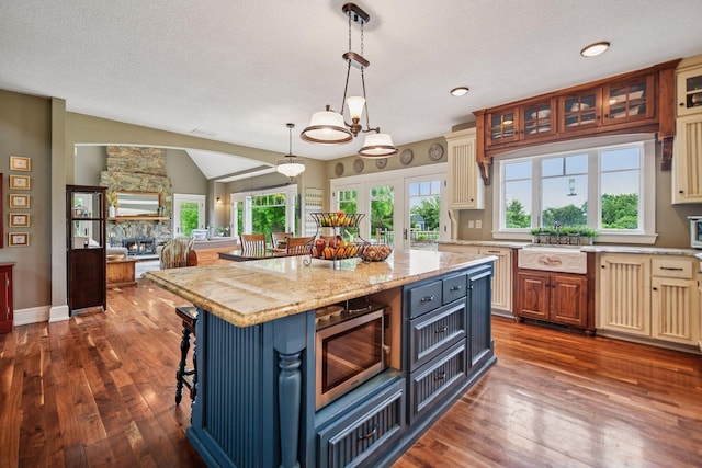 1755 Chateau Way, Minnetrista, MN 55359 - kitchen with stainless steel microwave, dark wood finished floors, glass insert cabinets, a center island, and decorative light fixtures