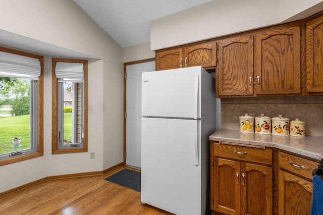 4540 Niagara Ln N, Plymouth, MN 55446 - kitchen featuring freestanding refrigerator, brown cabinetry, vaulted ceiling, light wood-style flooring, and decorative backsplash