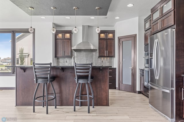 3004 6th St E, West Fargo, ND 58078 - kitchen featuring appliances with stainless steel finishes, wall chimney exhaust hood, dark countertops, light wood-style floors, and a breakfast bar area