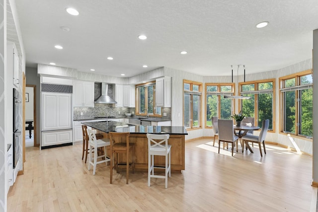 18715 24th Ave N, Plymouth, MN 55447 - kitchen featuring wall chimney range hood, light wood finished floors, a kitchen island, a kitchen bar, and white cabinets