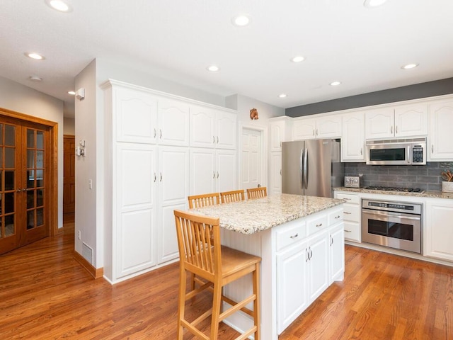 1776 Lockridge Ct, Waconia, MN 55387 - kitchen with stainless steel appliances, a kitchen breakfast bar, light wood finished floors, white cabinetry, and light stone countertops