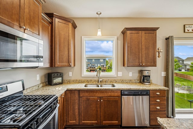 12083 79th St NE, Otsego, MN 55330 - kitchen with appliances with stainless steel finishes, a sink, light stone counters, hanging light fixtures, and brown cabinetry