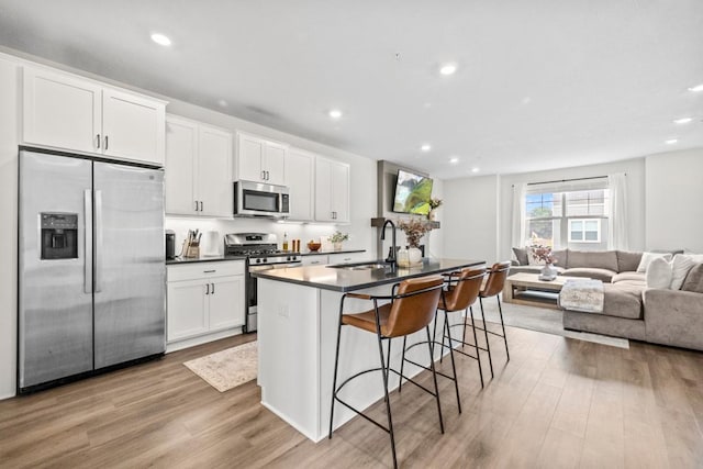1517 Timberwood Ln, West Saint Paul, MN 55118 - kitchen featuring appliances with stainless steel finishes, open floor plan, light wood-type flooring, white cabinetry, and a kitchen island with sink