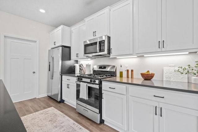 1517 Timberwood Ln, West Saint Paul, MN 55118 - kitchen featuring appliances with stainless steel finishes, white cabinetry, light wood-type flooring, dark countertops, and recessed lighting