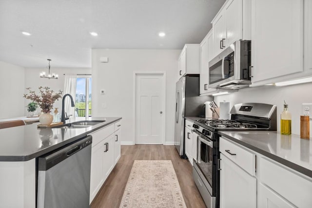 1517 Timberwood Ln, West Saint Paul, MN 55118 - kitchen with appliances with stainless steel finishes, dark countertops, a kitchen island with sink, a chandelier, and white cabinetry