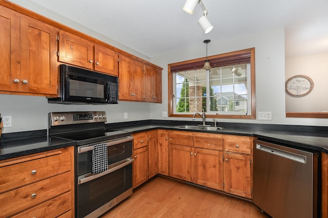 29259 Wildwood Rd, Chisago City, MN 55013 - kitchen with stainless steel appliances, brown cabinetry, light wood finished floors, dark countertops, and hanging light fixtures