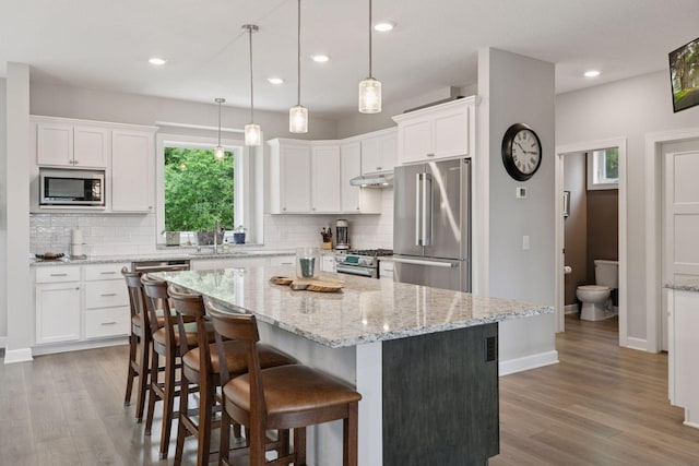 7465 Glengarry Pl, Eden Prairie, MN 55344 - kitchen featuring appliances with stainless steel finishes, under cabinet range hood, backsplash, wood finished floors, and recessed lighting