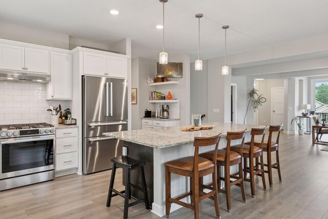 7465 Glengarry Pl, Eden Prairie, MN 55344 - kitchen featuring appliances with stainless steel finishes, under cabinet range hood, light wood-type flooring, decorative backsplash, and a kitchen island