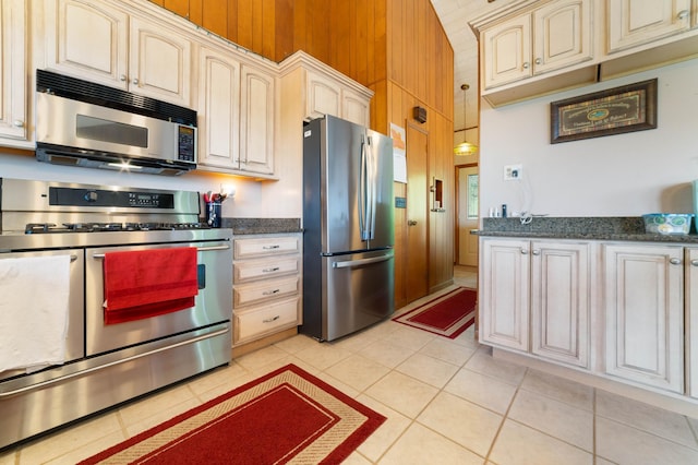 1928 Loop Rd, Two Harbors, MN 55616 - kitchen featuring appliances with stainless steel finishes, cream cabinets, light tile patterned floors, dark stone counters, and wooden walls