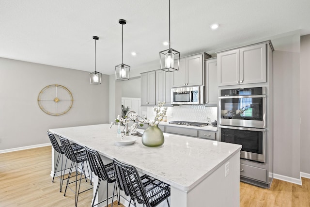 14645 Cloquet St, Dayton, MN 55327 - kitchen featuring stainless steel appliances, light wood finished floors, light stone countertops, an island with sink, and tasteful backsplash