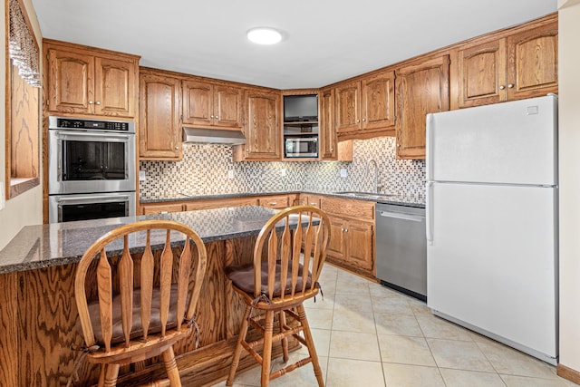 17000 Jackal St NW, Ramsey, MN 55303 - kitchen with stainless steel appliances, under cabinet range hood, backsplash, light tile patterned flooring, and brown cabinets