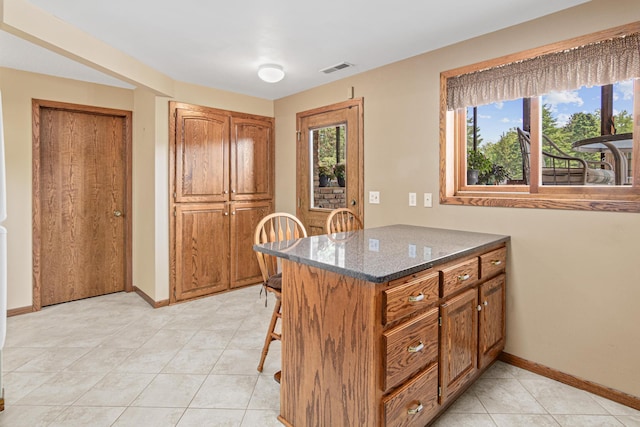 17000 Jackal St NW, Ramsey, MN 55303 - kitchen with brown cabinetry, dark stone counters, a breakfast bar area, light tile patterned floors, and a peninsula