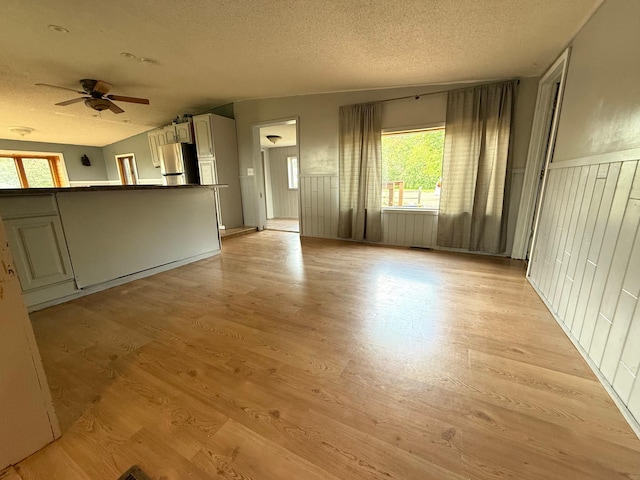 110 9th Ave NE, Deer River, MN 56636 - unfurnished living room featuring a textured ceiling, a ceiling fan, light wood-type flooring, and a wainscoted wall