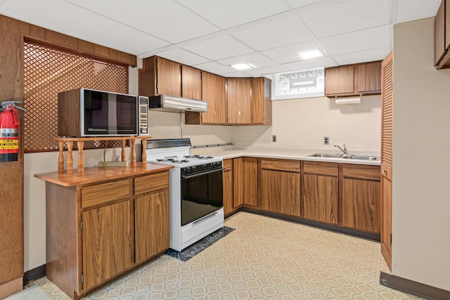 148 5th Ave N, Hopkins, MN 55343 - kitchen featuring white range with gas cooktop, wall chimney exhaust hood, brown cabinetry, a drop ceiling, and light countertops