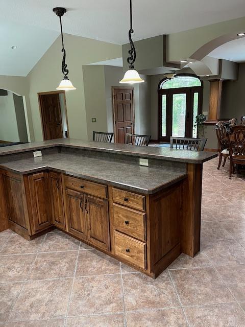 23567 Timber Trail Dr, Bemidji, MN 56601 - kitchen featuring dark countertops, light tile patterned floors, arched walkways, lofted ceiling, and hanging light fixtures