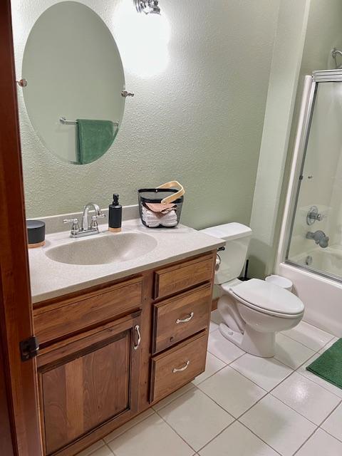23567 Timber Trail Dr, Bemidji, MN 56601 - bathroom with vanity, tile patterned flooring, toilet, shower / bath combination with glass door, and a textured wall